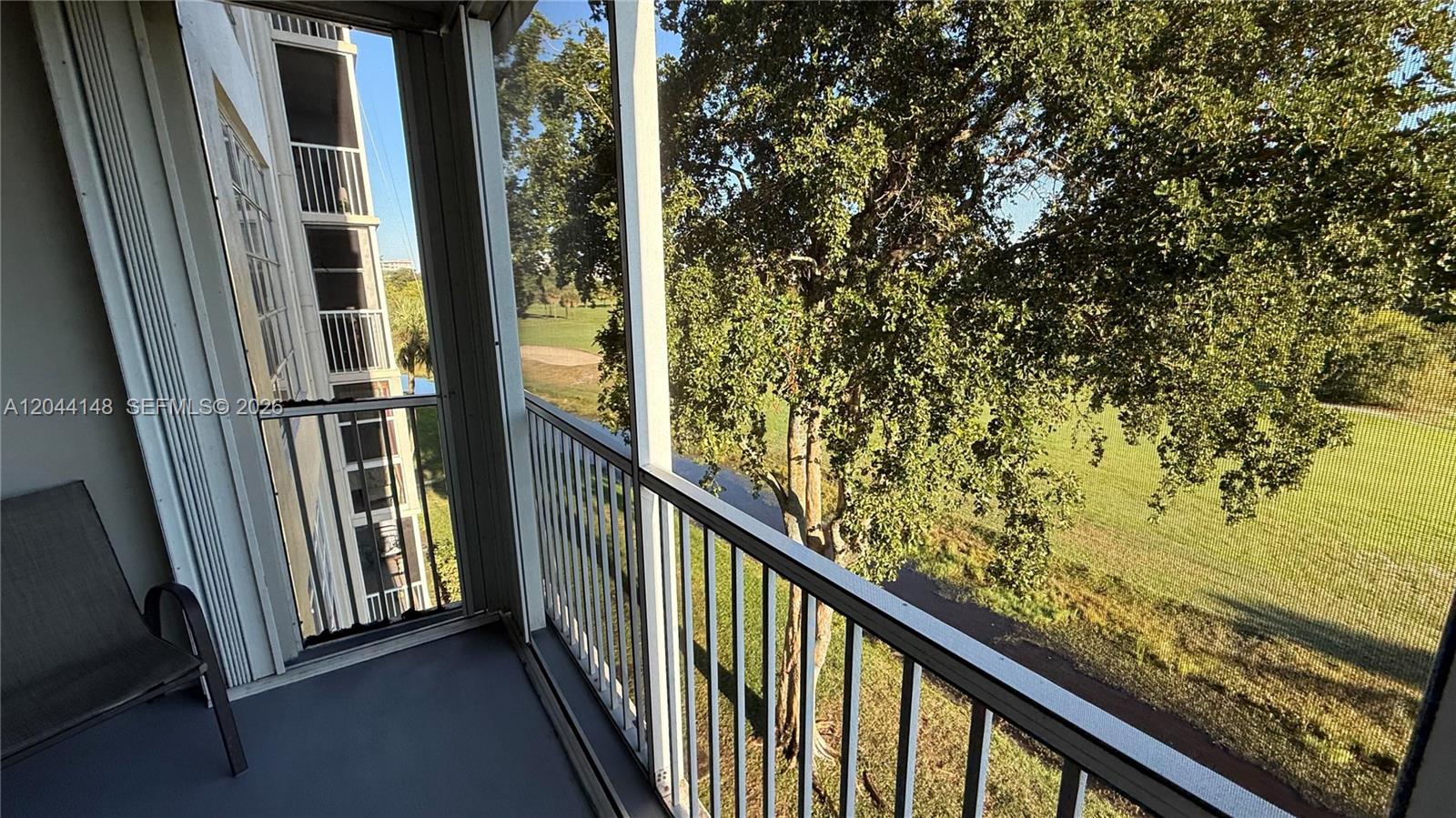 A screened-in balcony overlooks a grassy area with a large tree and a building — 2901 S Palm Aire Dr # 408, Pompano Beach FL 33069, POMPANO BEACH, FL