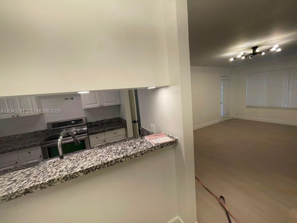 A kitchen with granite countertops overlooks an adjacent living area with a ceiling light fixture — 4341 W Mcnab Rd # 21, Pompano Beach FL 33069, POMPANO BEACH, FL