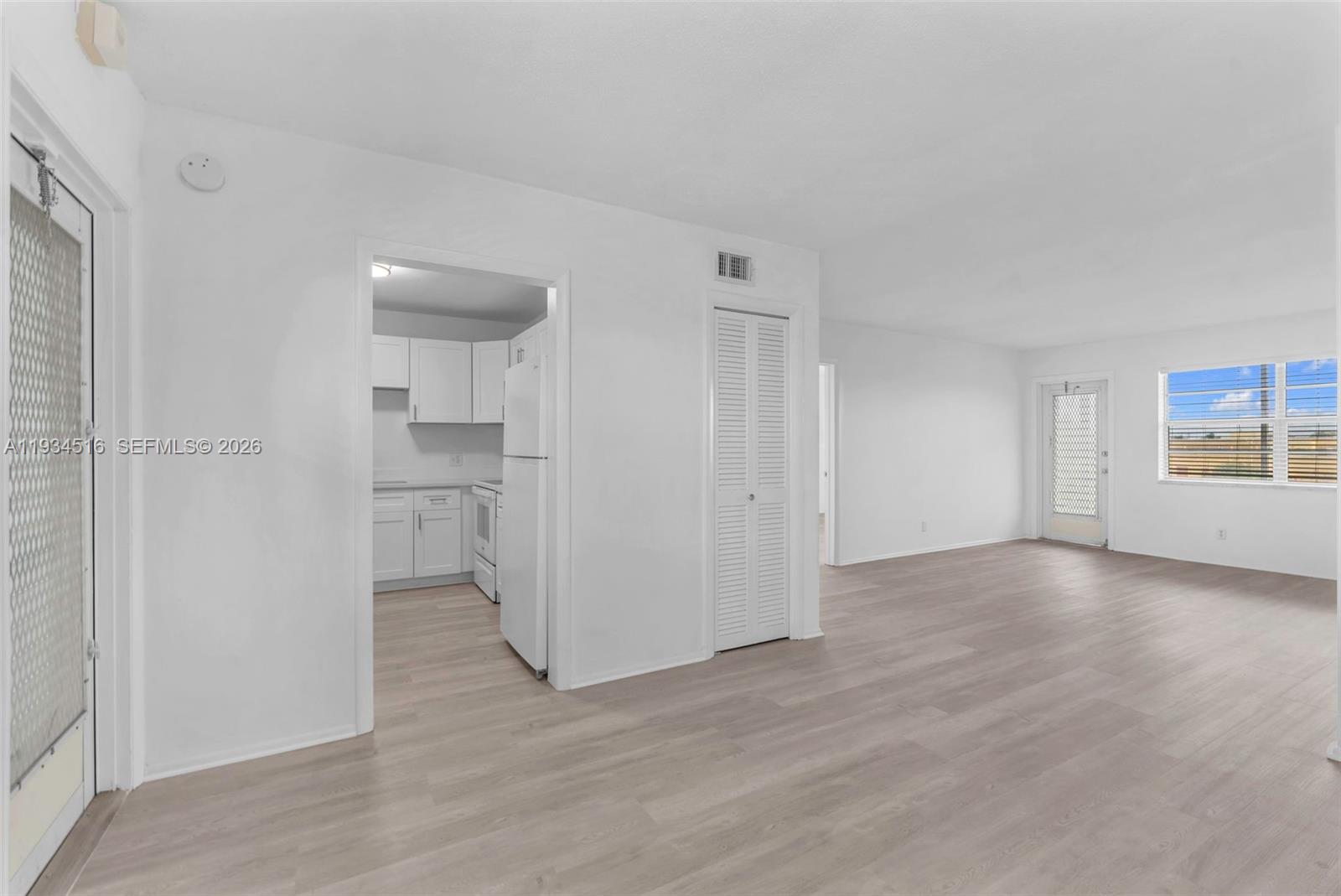 A bright living area with light wood-look flooring leads into a white kitchen — 1280 NW 43rd Ave # 302, Lauderhill FL 33313, LAUDERHILL, FL