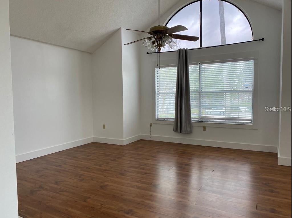 A living room with vaulted ceilings, wood-look flooring, a ceiling fan, and large windows — 3127 FOX SQUIRREL DRIVE UNIT 3127, KISSIMMEE, FL