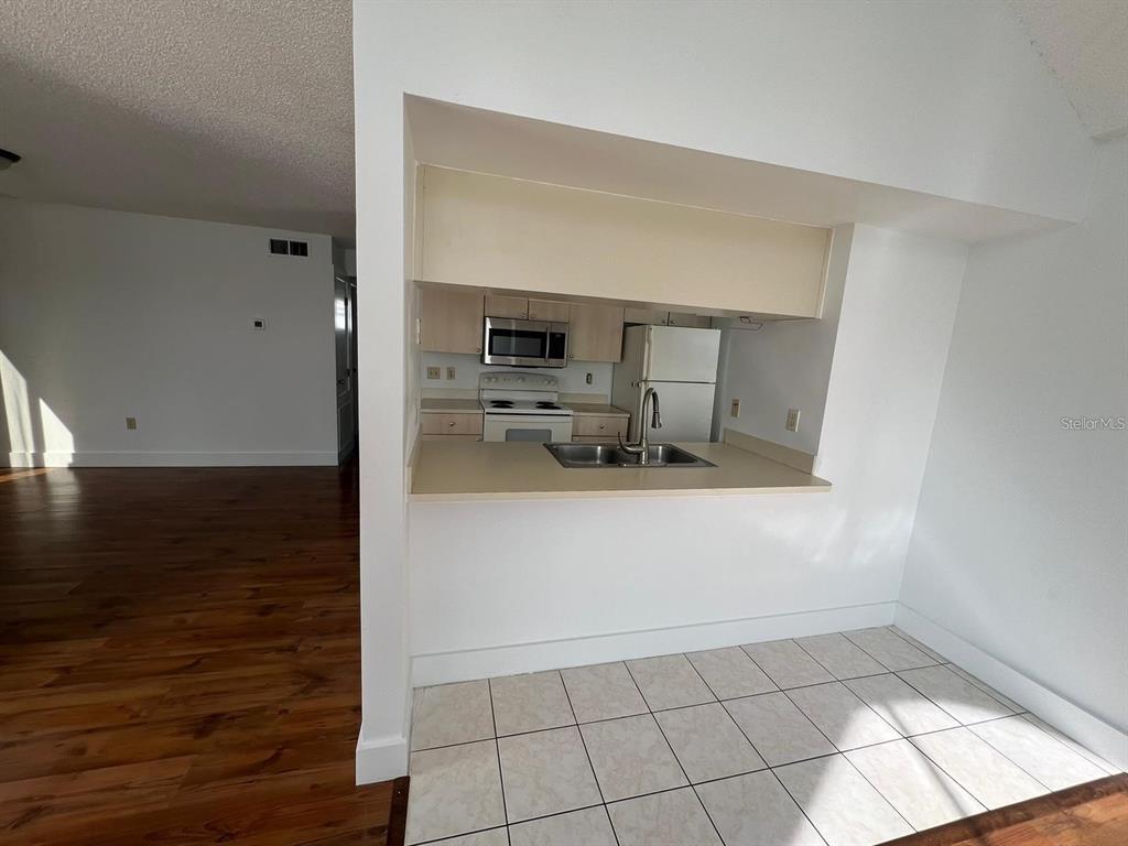 A kitchen with light-colored cabinets and appliances overlooks a tiled dining area — 3127 FOX SQUIRREL DRIVE UNIT 3127, KISSIMMEE, FL