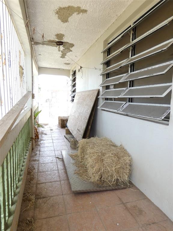 A covered outdoor porch features tiled flooring, louvered windows, and water-damaged ceiling plaster — 491 CALLE GLADIOLA, VIEQUES, PR
