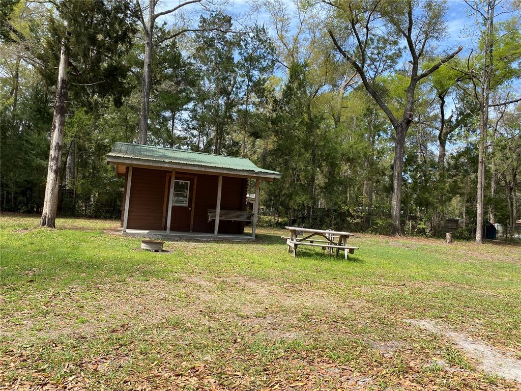 A small wooden cabin with a green metal roof sits in a grassy, wooded area — 8587 SW ELIM CHURCH ROAD, FORT WHITE, FL