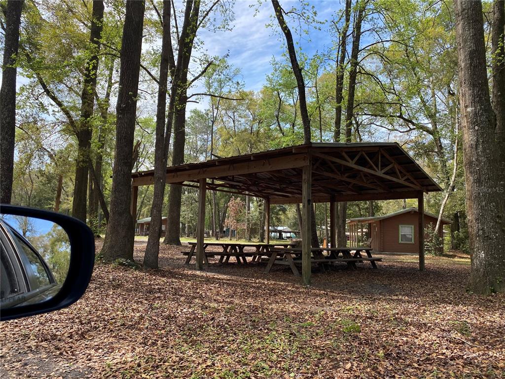 A wooden pavilion with picnic tables stands in a wooded area near small cabins — 8587 SW ELIM CHURCH ROAD, FORT WHITE, FL