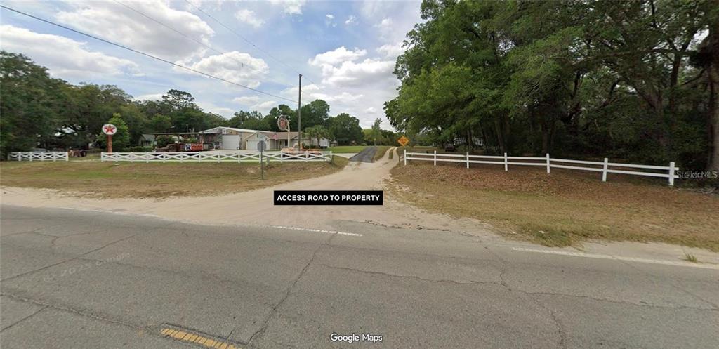 A gravel driveway leads from a paved road toward a property with white fencing — TBD SE 71ST TERRACE ROAD, BELLEVIEW, FL