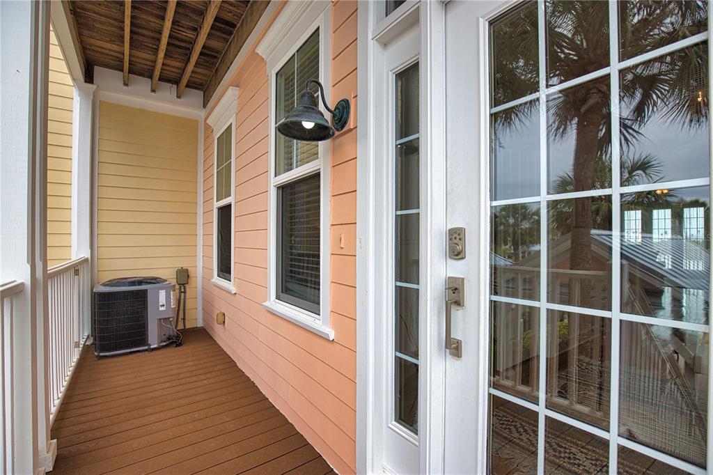 A wooden deck balcony features peach-colored siding, a glass-paned door, and an outdoor air conditioner — 11723 ANGLERS CLUB DRIVE UNIT 131, PLACIDA, FL