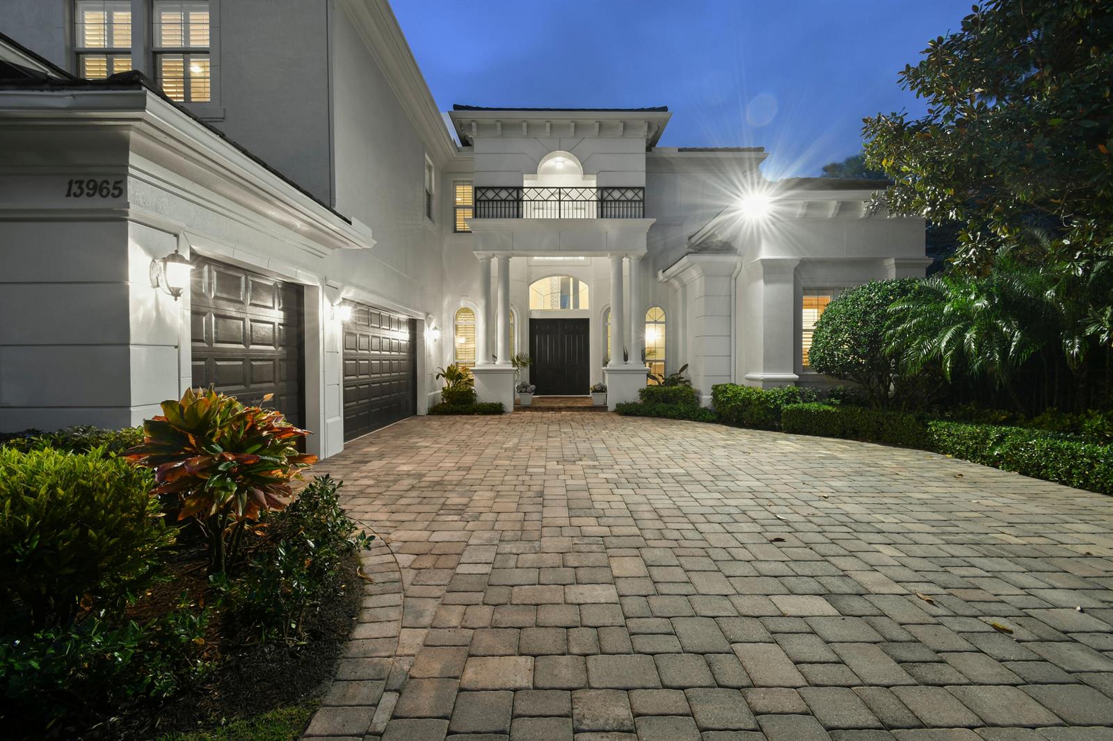 A white two-story house with a paved driveway, dark garage doors, and a balcony at night — 13965 Willow Cay Drive, Juno Beach FL 33408, JUNO BEACH, FL
