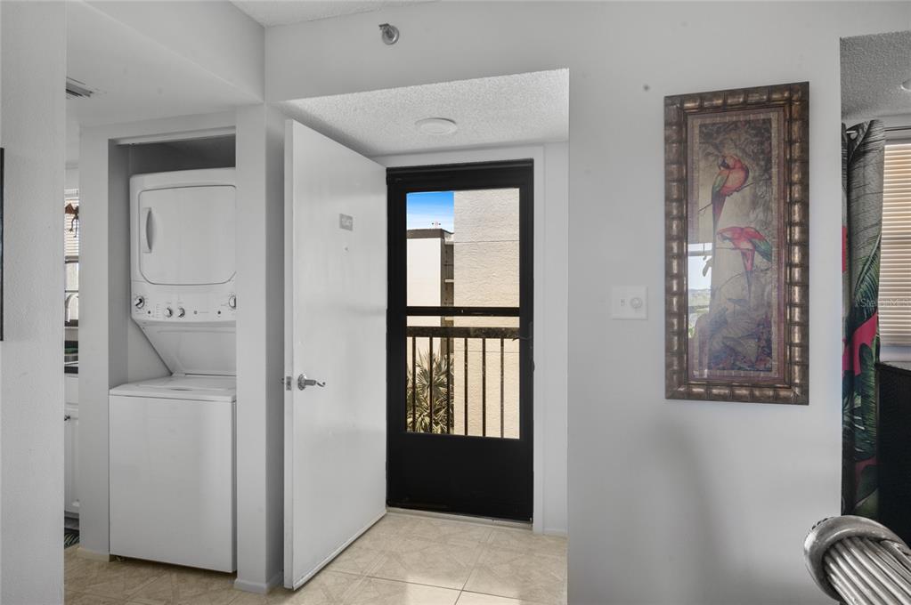 A white stacked washer and dryer unit sits next to an open door leading outside — 9860 62ND TERRACE N UNIT 1047, ST PETERSBURG, FL