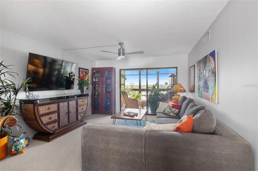 A living room features a grey sectional sofa, a wooden media console, and a sliding door — 9860 62ND TERRACE N UNIT 1047, ST PETERSBURG, FL
