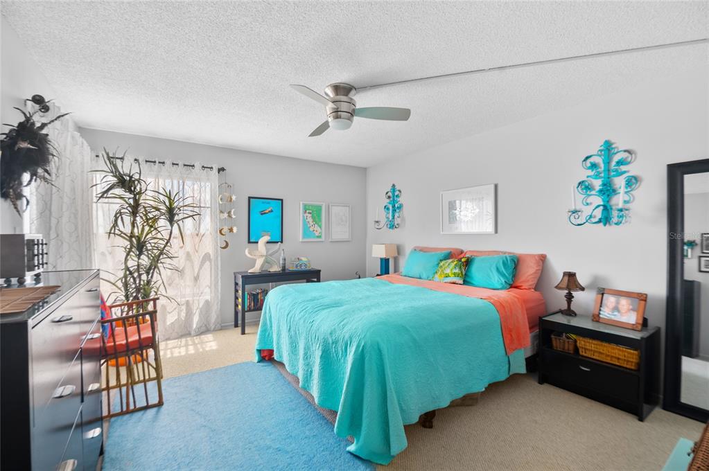 A bedroom features a bed with a turquoise quilt, a ceiling fan, and a large window — 9860 62ND TERRACE N UNIT 1047, ST PETERSBURG, FL