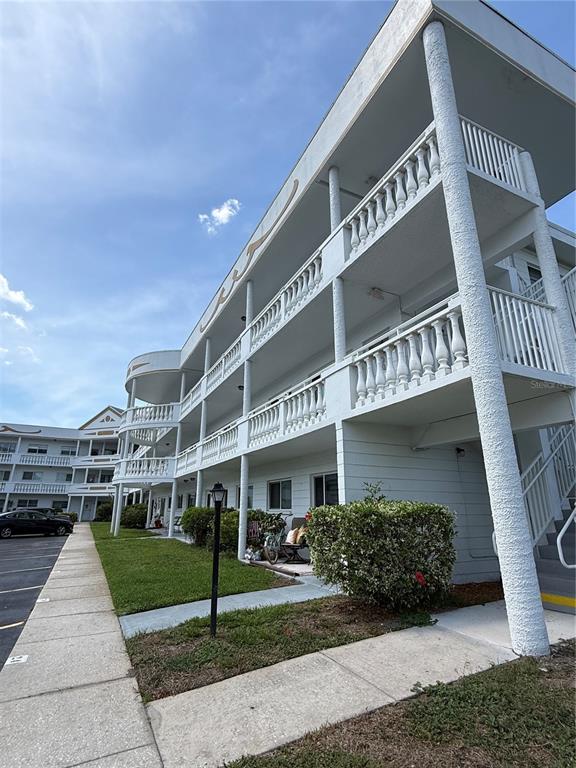 A multi-story white apartment building features exterior walkways with balustrade railings and concrete pillars — 2428 COLUMBIA DRIVE UNIT 68, CLEARWATER, FL