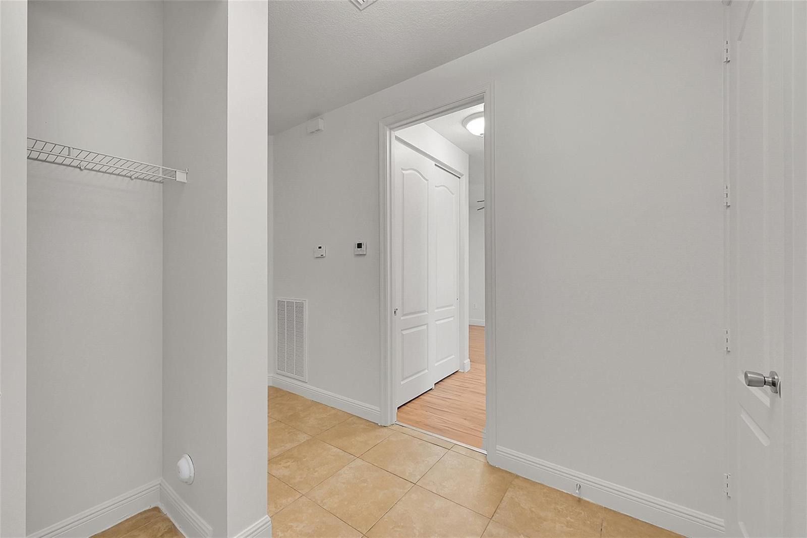 A hallway with beige tile flooring leads to a doorway revealing a room with wood flooring — 3605 NW 5th Terrace, Boca Raton FL 33431, BOCA RATON, FL