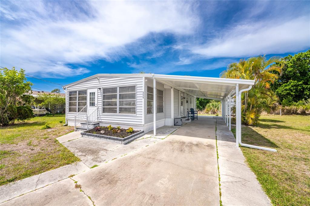 A single-story mobile home with white siding, a concrete driveway, and an attached carport — 258 VIA DE LUNA, ENGLEWOOD, FL