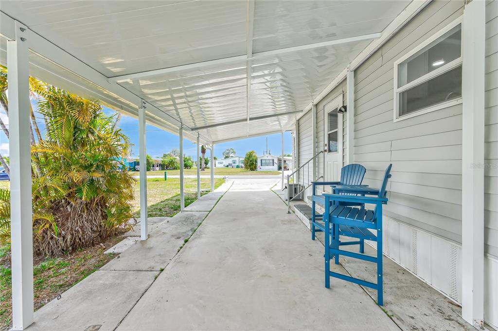 A covered concrete carport area sits beside a light gray mobile home with blue chairs — 258 VIA DE LUNA, ENGLEWOOD, FL