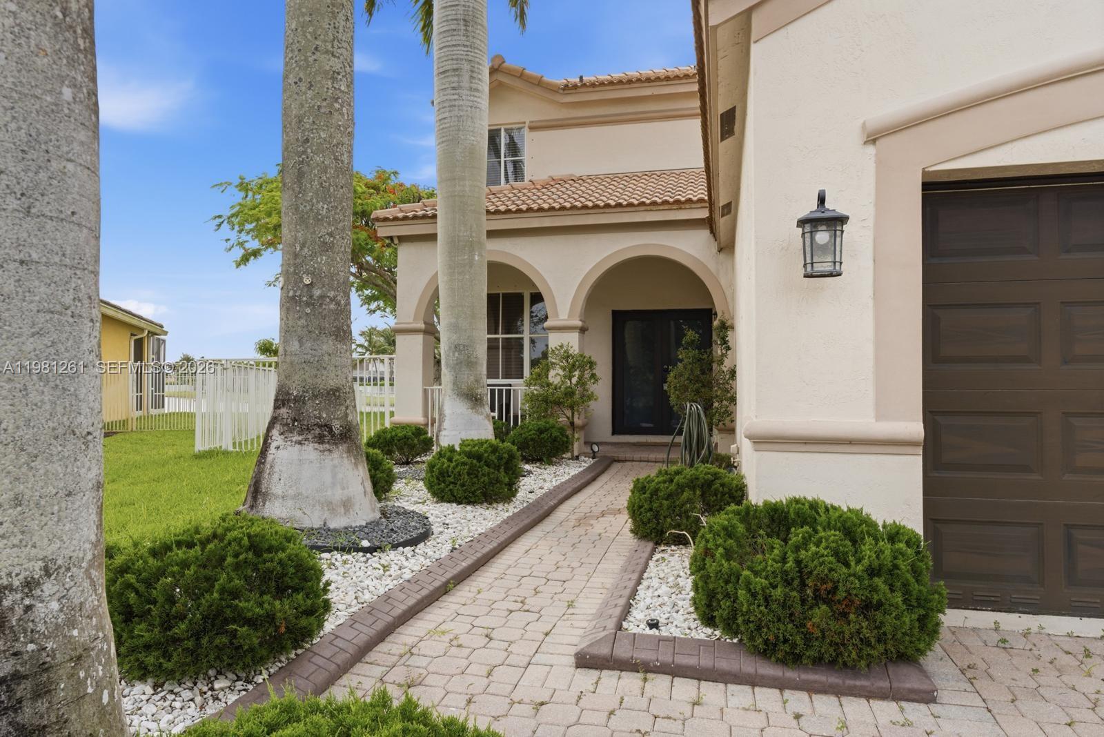 A paved walkway leads to the arched entryway of a two-story stucco house with palm trees — 663 Live Oak Ln, Weston FL 33327, WESTON, FL