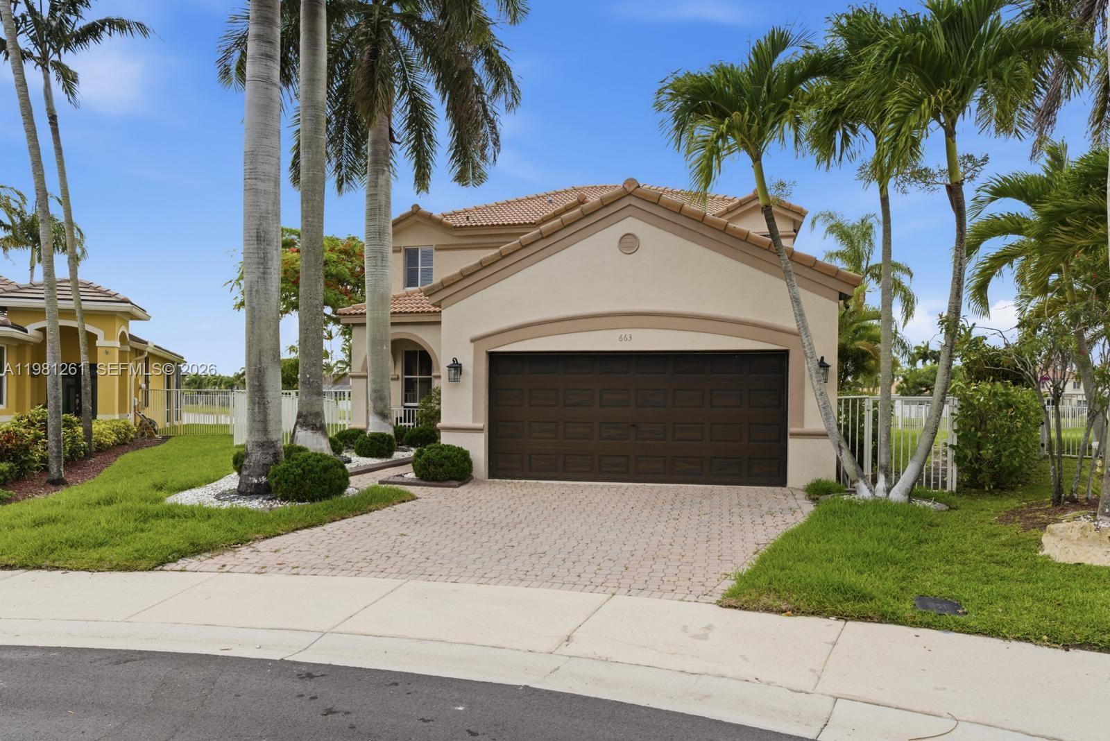 A two-story house with a beige stucco exterior, a dark garage door, and palm trees — 663 Live Oak Ln, Weston FL 33327, WESTON, FL