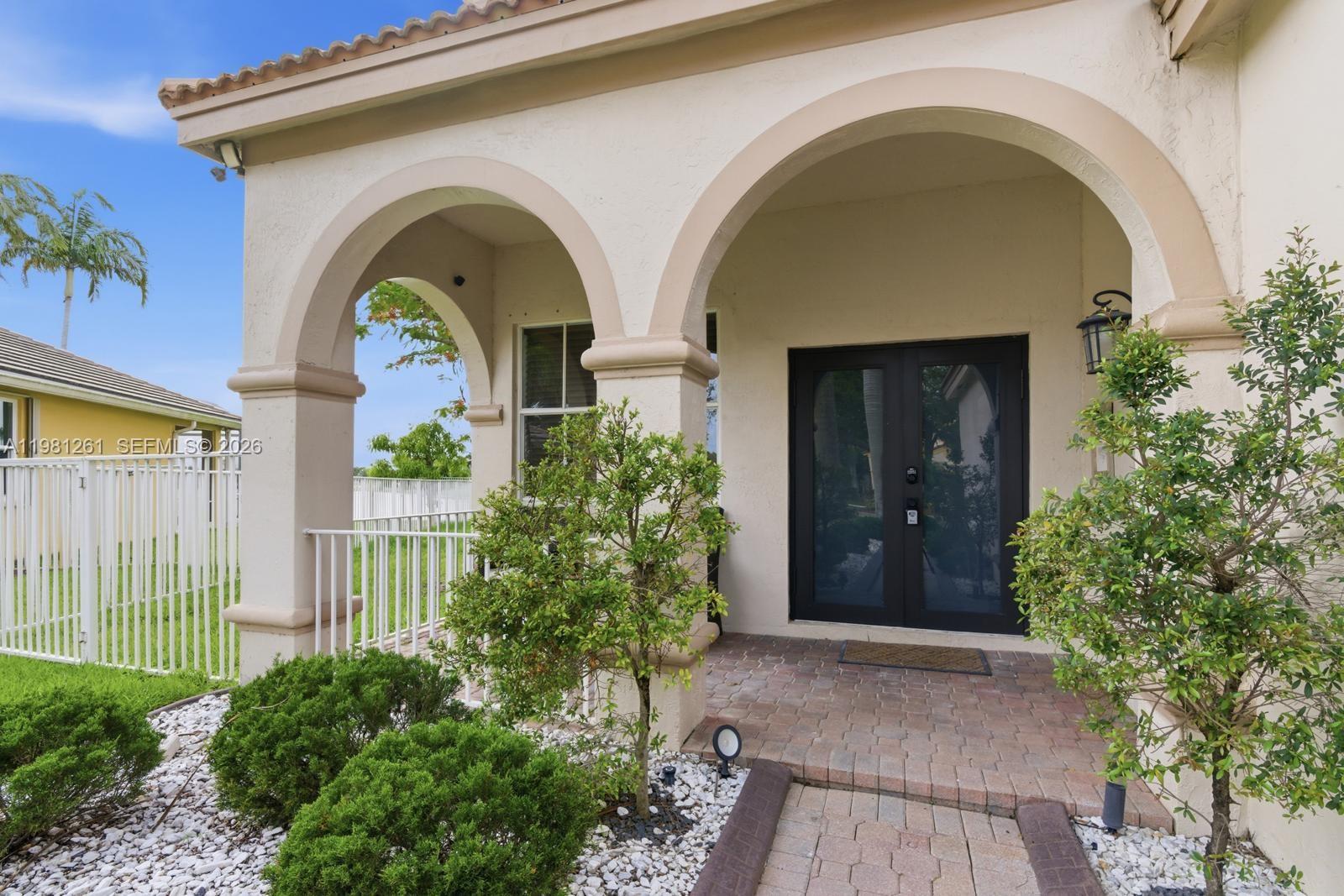 The exterior of a house features a covered arched entryway with a brick walkway — 663 Live Oak Ln, Weston FL 33327, WESTON, FL