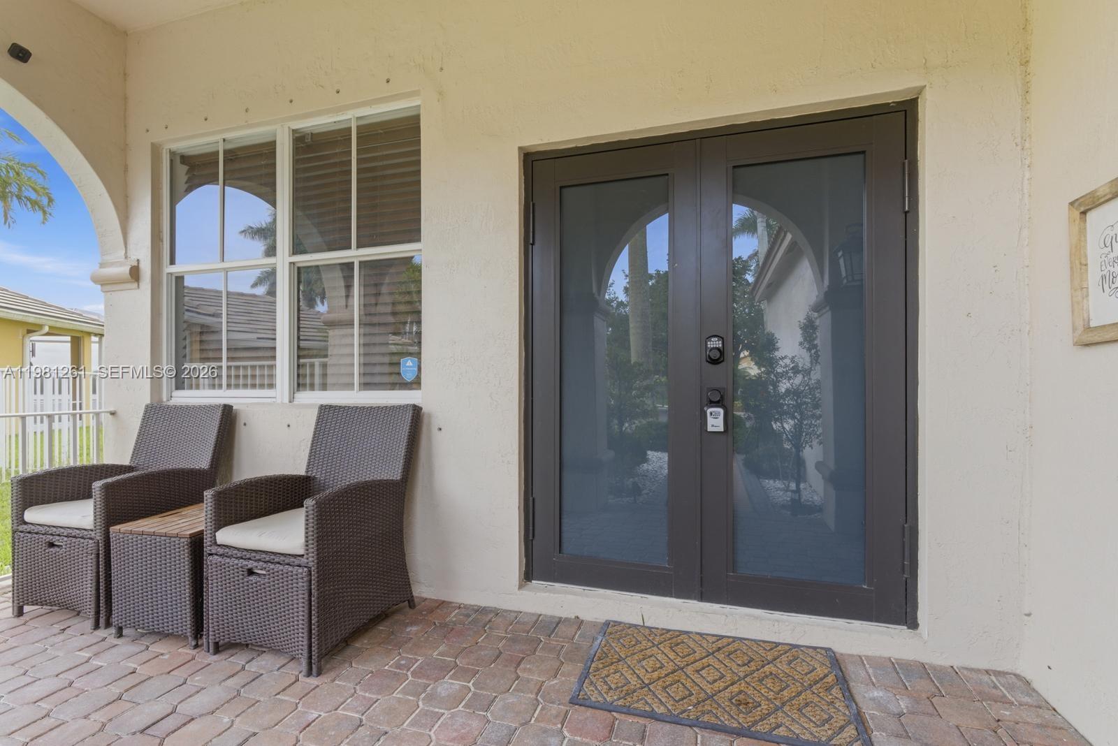 A covered patio features two wicker chairs, a small table, and double glass doors — 663 Live Oak Ln, Weston FL 33327, WESTON, FL