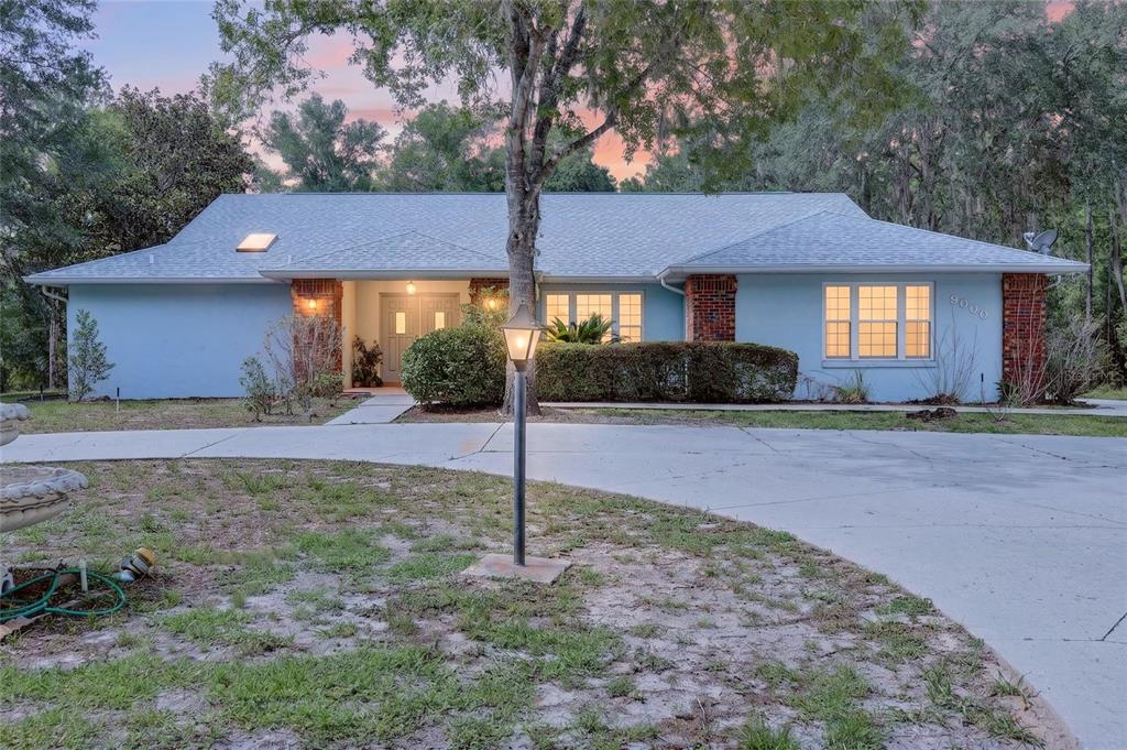 A light blue single-story house features a brick entryway, a circular driveway, and a lawn — 9000 SW 203RD COURT, DUNNELLON, FL