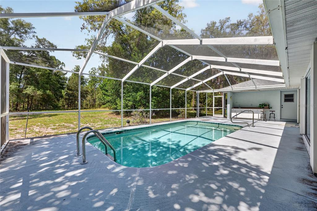 A screened-in swimming pool with a concrete deck and an outdoor bar area — 9000 SW 203RD COURT, DUNNELLON, FL