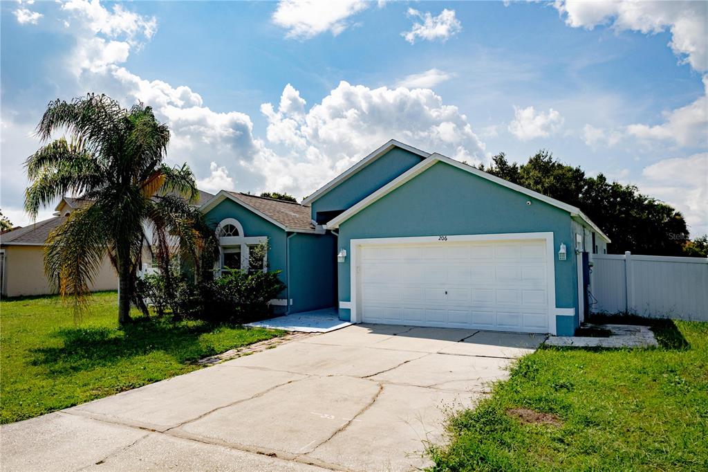 A blue single-story house with a two-car garage and a palm tree in the front yard — 206 GREAT YARMOUTH COURT, KISSIMMEE, FL