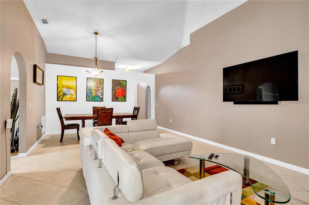 A living room with a white sectional sofa, a dining area, and a wall-mounted television — 206 GREAT YARMOUTH COURT, KISSIMMEE, FL