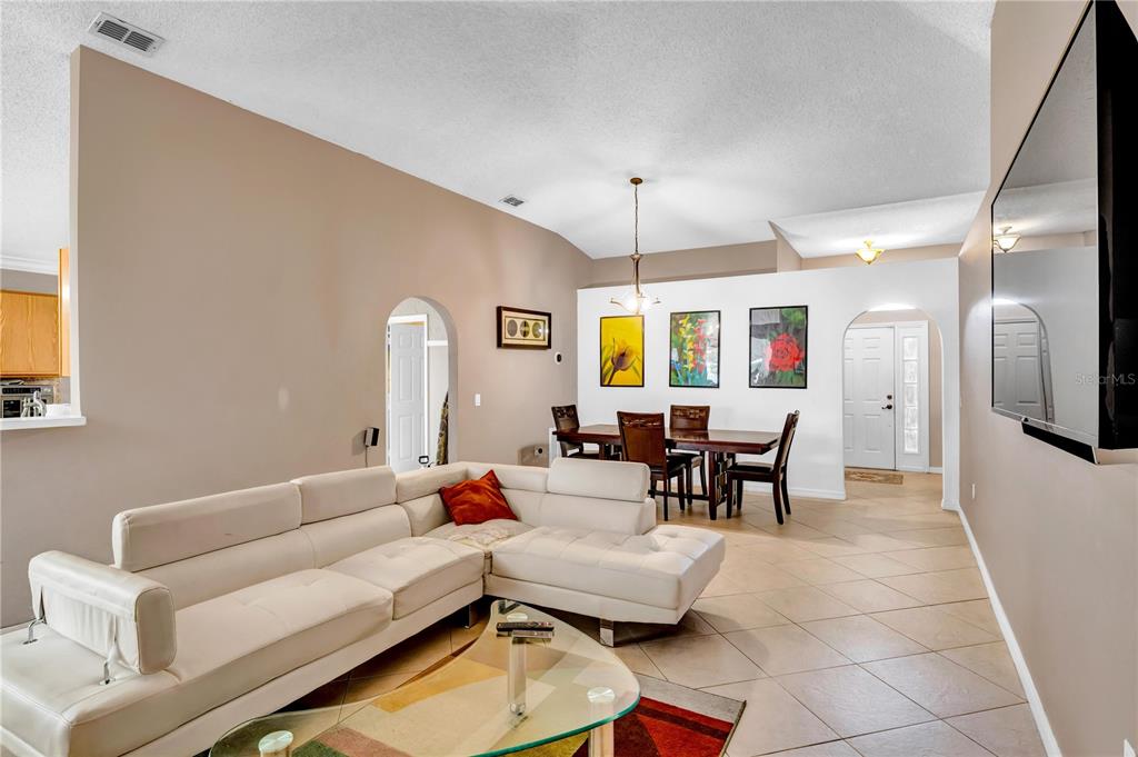 A living room with a white sectional sofa, glass coffee table, and adjacent dining area — 206 GREAT YARMOUTH COURT, KISSIMMEE, FL