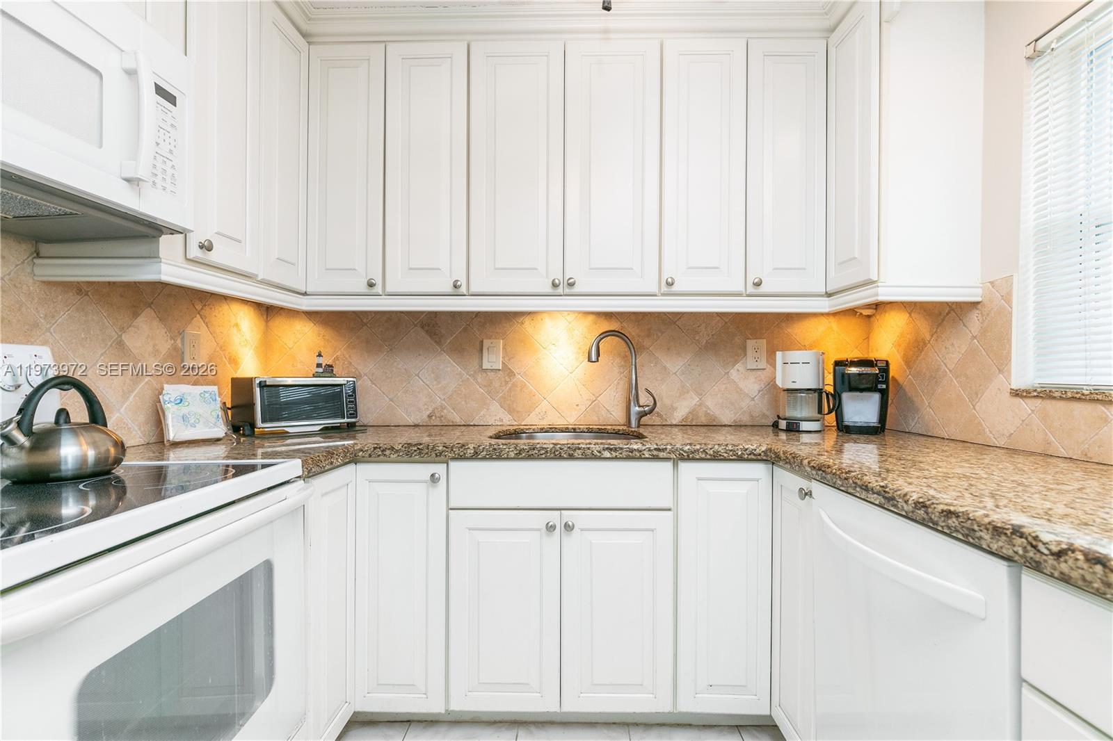 A kitchen features white cabinets, granite countertops, a tiled backsplash, and stainless steel appliances — 3131 S Ocean Dr # 110, Hallandale Beach FL 33009, HALLANDALE BEACH, FL