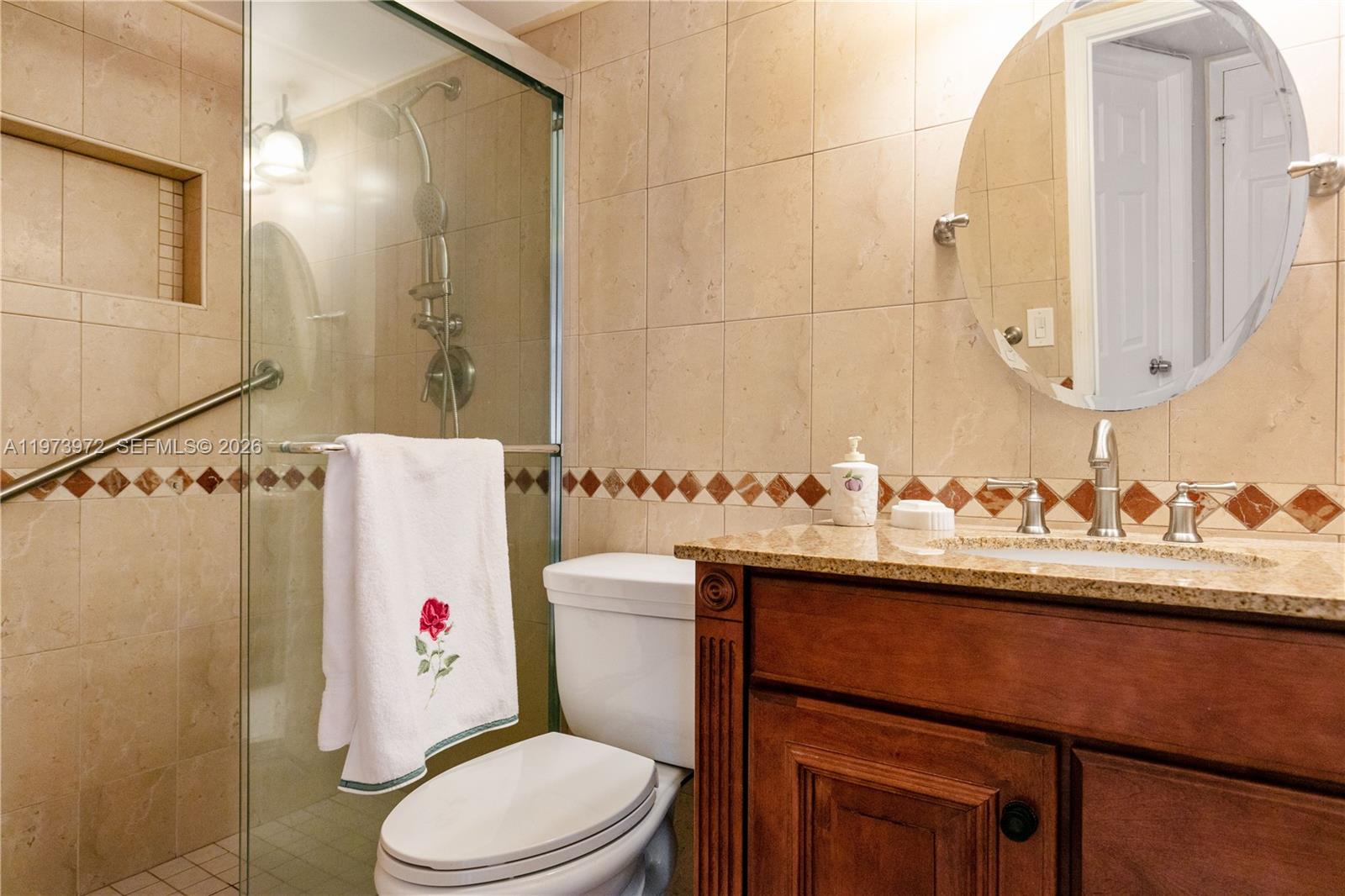 A bathroom features a glass-enclosed shower, a wood vanity with granite countertop, and beige tiling — 3131 S Ocean Dr # 110, Hallandale Beach FL 33009, HALLANDALE BEACH, FL