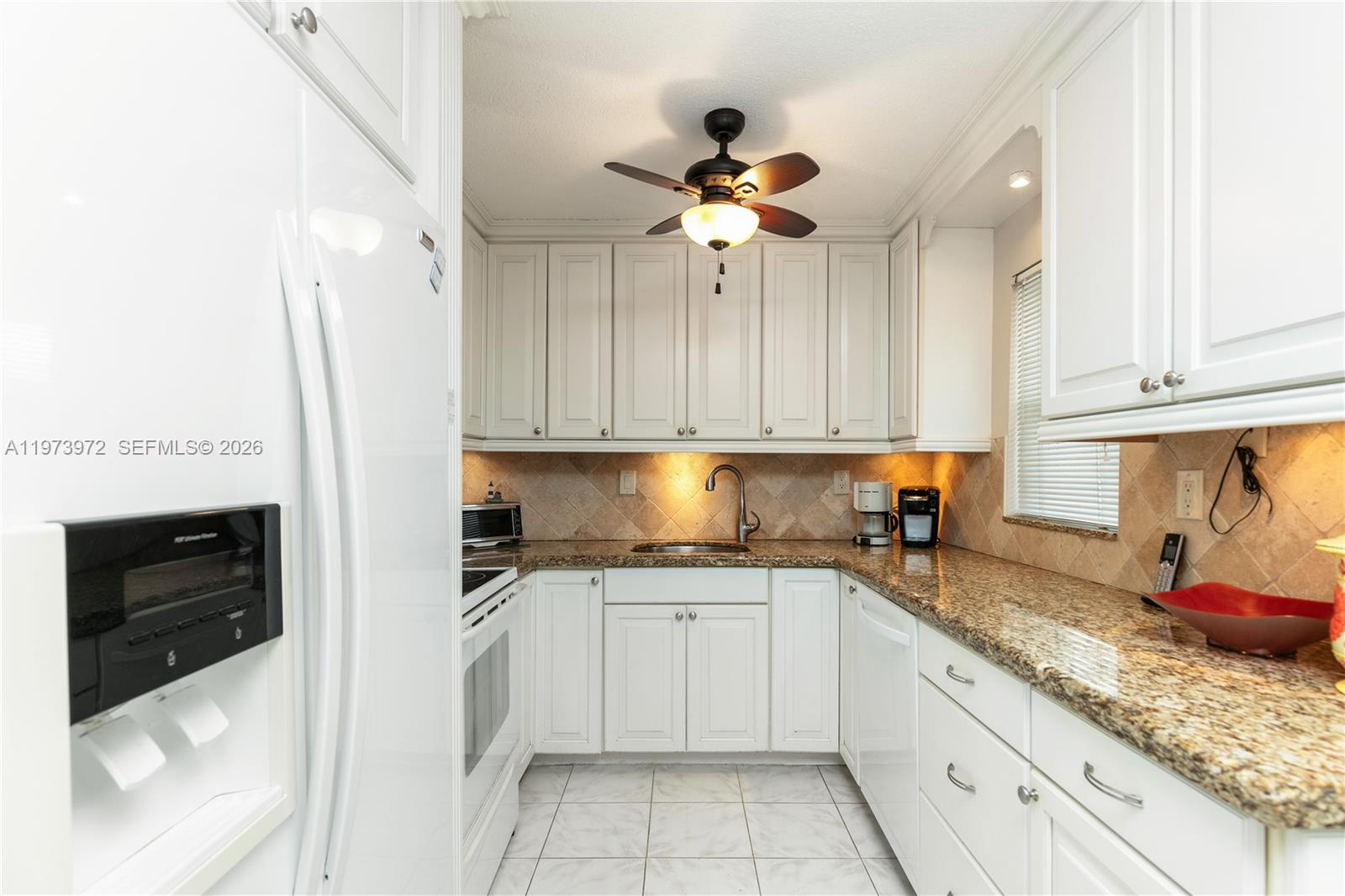 A kitchen features white cabinets, granite countertops, a tiled backsplash, and a ceiling fan — 3131 S Ocean Dr # 110, Hallandale Beach FL 33009, HALLANDALE BEACH, FL