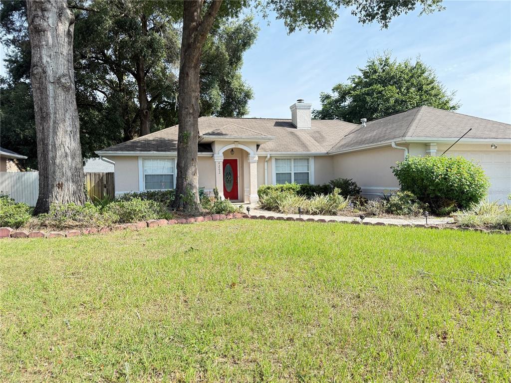 A single-story house with a red front door, beige siding, and a large front lawn — 4262 NE 35TH AVENUE ROAD, OCALA, FL
