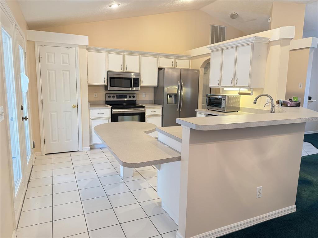 A kitchen with white cabinets, stainless steel appliances, a breakfast bar, and white tile flooring — 4262 NE 35TH AVENUE ROAD, OCALA, FL
