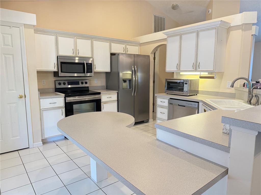 A kitchen features white cabinets, stainless steel appliances, a gray countertop, and white tile flooring — 4262 NE 35TH AVENUE ROAD, OCALA, FL