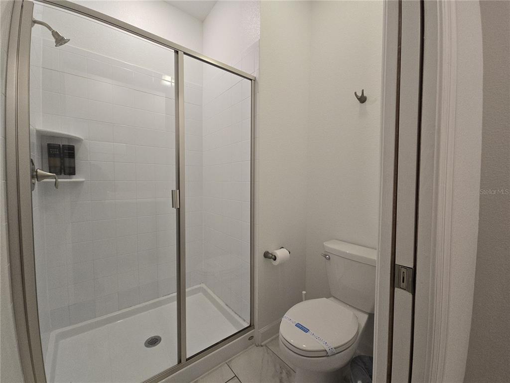 A bathroom features a glass-enclosed walk-in shower with white tile and a white toilet — 1036 LEADER STREET, DAVENPORT, FL