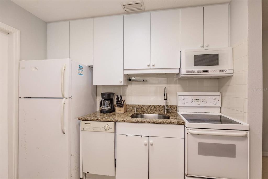 A kitchen features white cabinets, a granite countertop, a white refrigerator, and a white stove — 6020 MIDNIGHT PASS ROAD UNIT 59, SARASOTA, FL