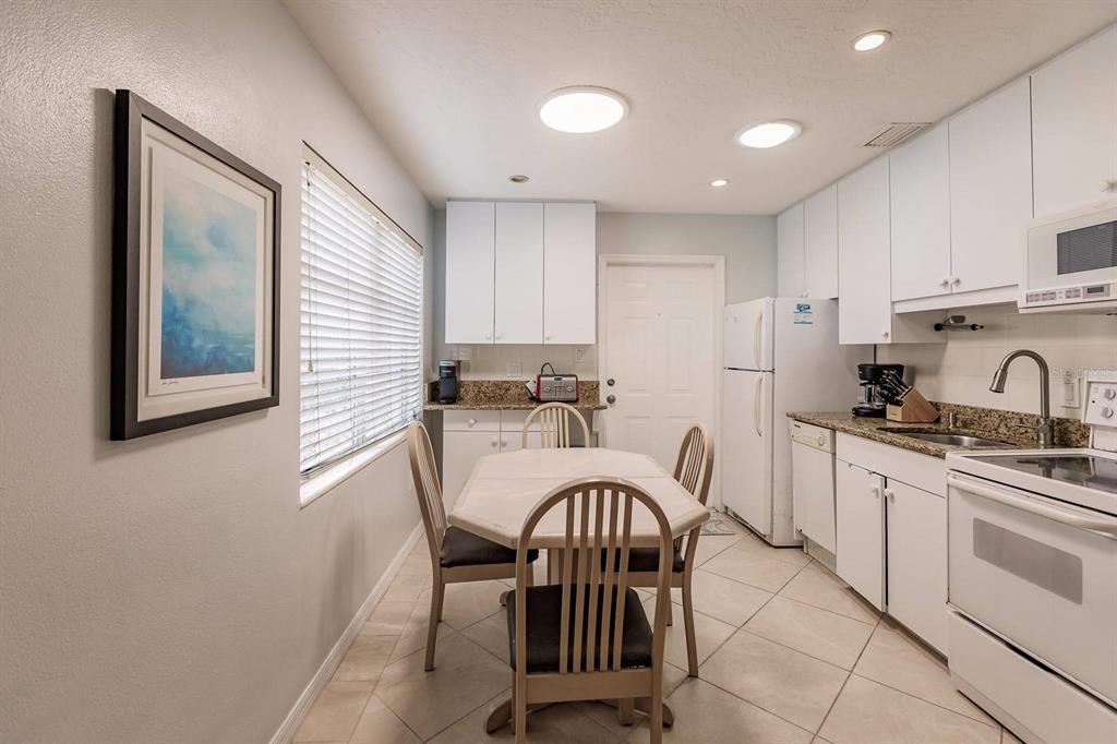 A kitchen with white cabinets, granite countertops, a dining table, and tile flooring — 6020 MIDNIGHT PASS ROAD UNIT 59, SARASOTA, FL