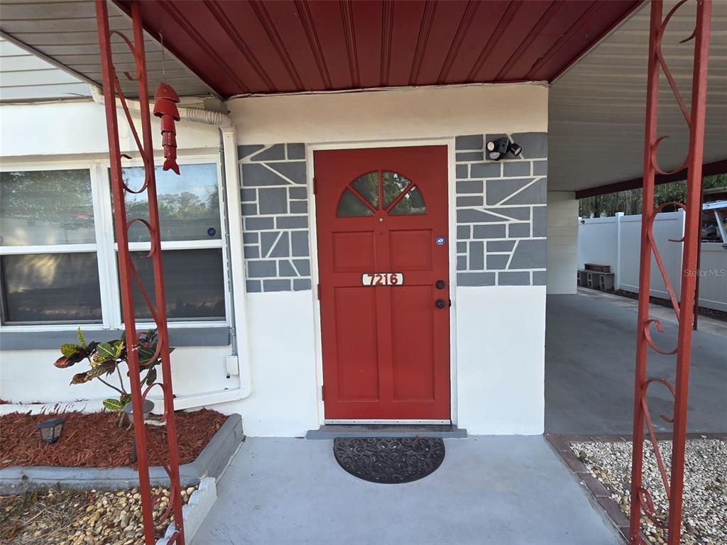 A red front door with a decorative window is centered on a white exterior wall — 7216 JAMES STREET, PORT RICHEY, FL