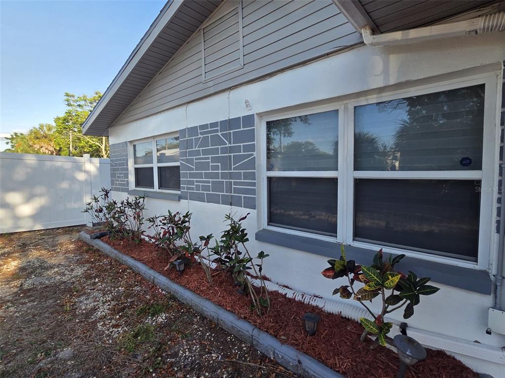 The exterior of a house features white stucco walls, gray stone accents, and a garden bed — 7216 JAMES STREET, PORT RICHEY, FL