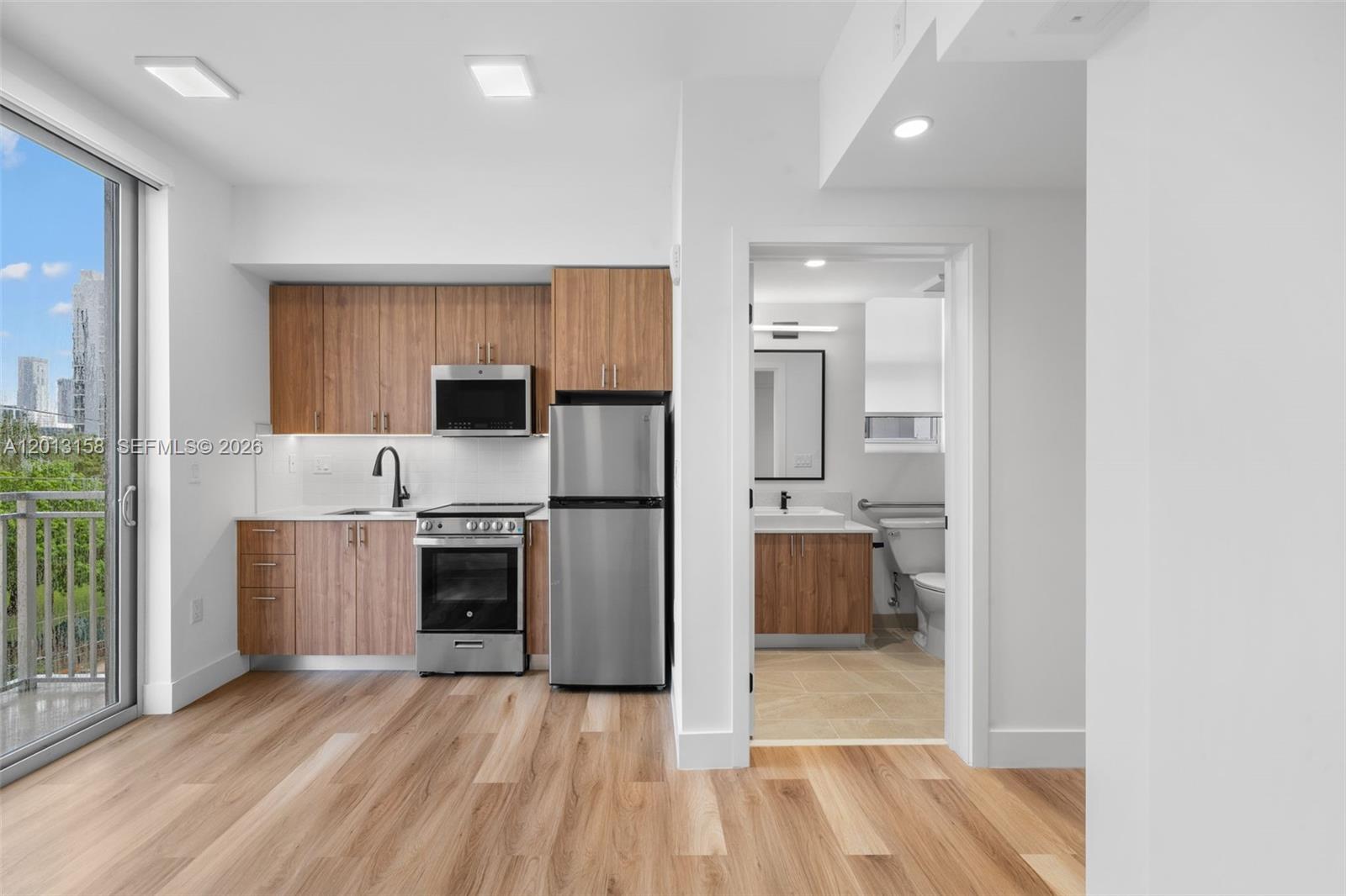 A kitchen with wood cabinets and stainless steel appliances sits next to a bathroom doorway — 650 SW 1st St # 206, Miami FL 33130, MIAMI, FL