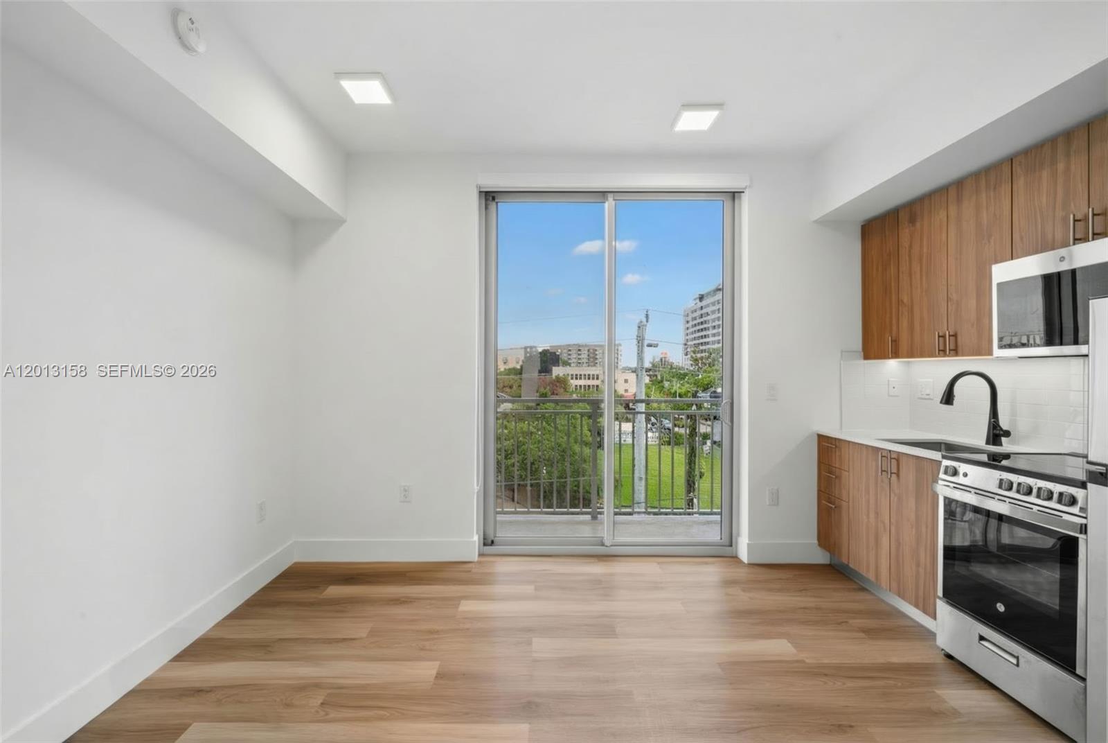 A modern kitchen and dining area features wood cabinets, stainless steel appliances, and a balcony — 650 SW 1st St # 206, Miami FL 33130, MIAMI, FL