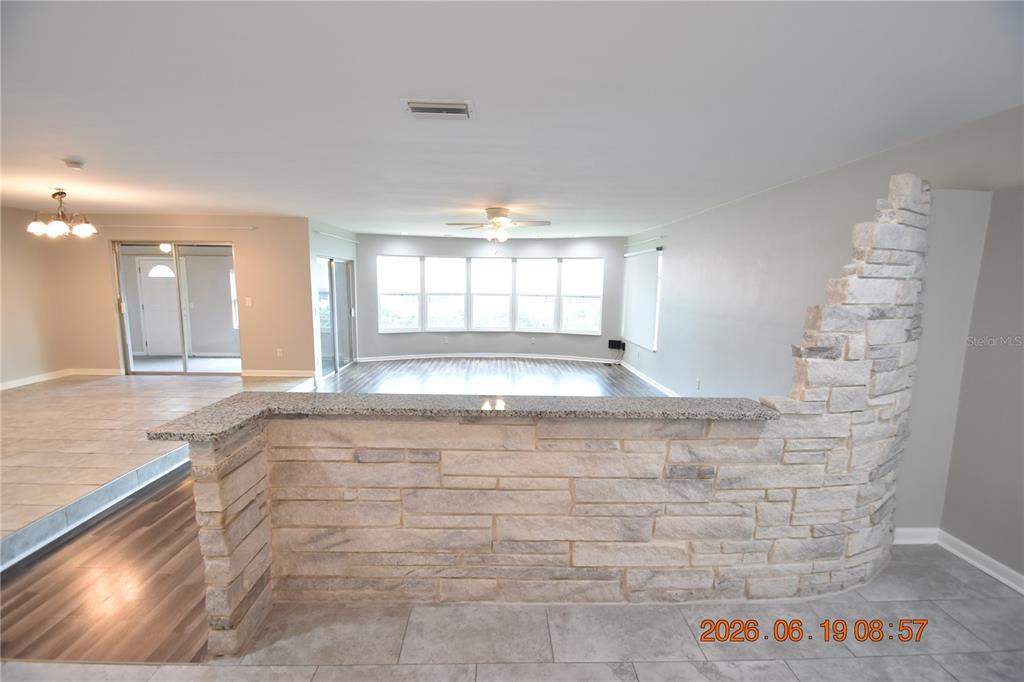 A stone-faced half wall separates a tiled kitchen area from a wood-floored living room — 3273 HARBOR LAKE DRIVE, LARGO, FL