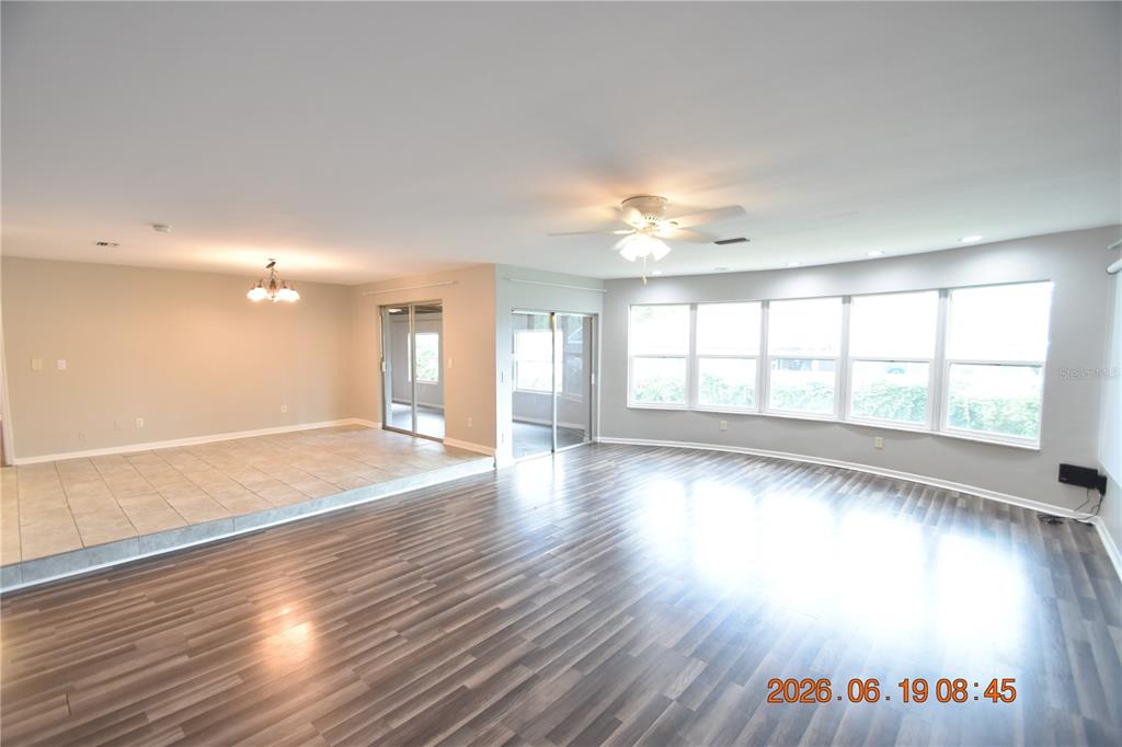 A spacious living area features wood-look flooring, a tiled raised section, and large windows — 3273 HARBOR LAKE DRIVE, LARGO, FL