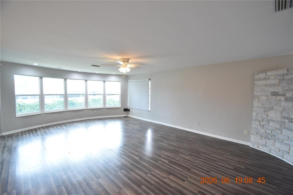 A spacious living room features dark wood-look flooring, light gray walls, and a stone fireplace — 3273 HARBOR LAKE DRIVE, LARGO, FL