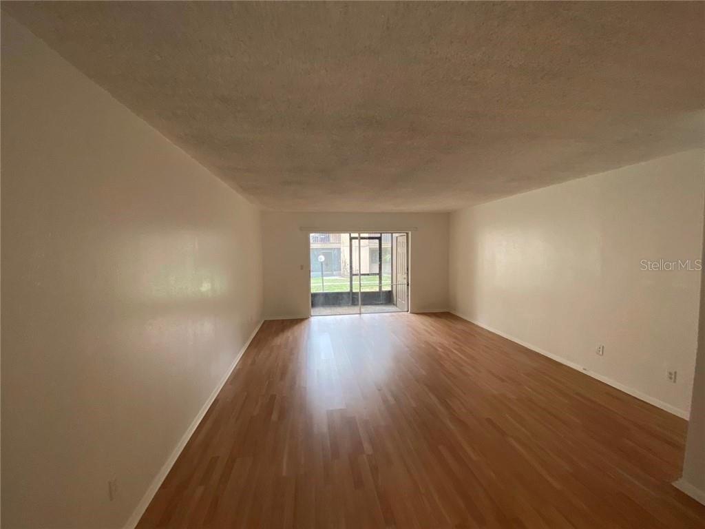 An empty living room features light wood-look flooring, white walls, and a sliding glass door — 7508 PRESLEY PLACE UNIT 100, TAMPA, FL