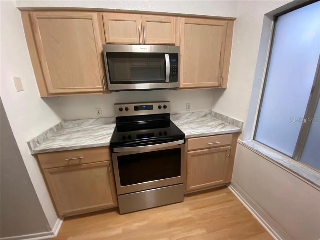 A kitchen features light wood cabinets, stainless steel appliances, and marble-patterned laminate countertops — 7508 PRESLEY PLACE UNIT 100, TAMPA, FL