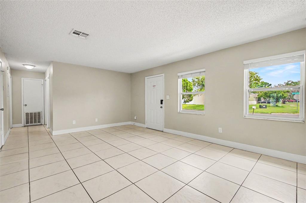 An empty room with beige walls, white tile flooring, a white door, and two windows — 140 GUAYMAS DRIVE, KISSIMMEE, FL