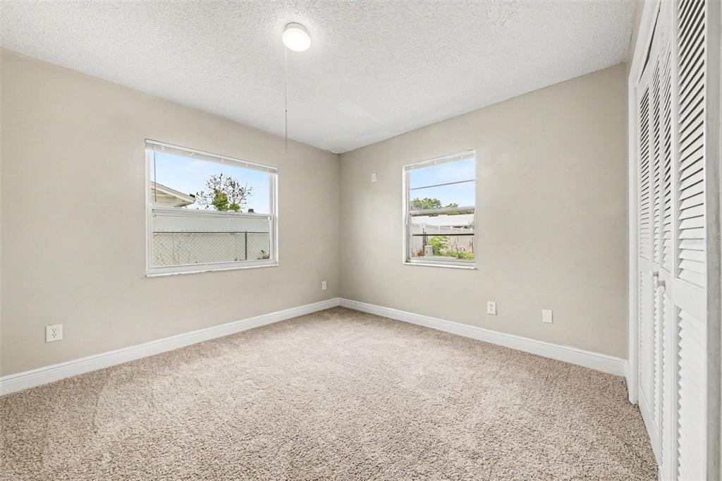 An empty bedroom features beige walls, tan carpeting, two windows, and white louvered closet doors — 140 GUAYMAS DRIVE, KISSIMMEE, FL