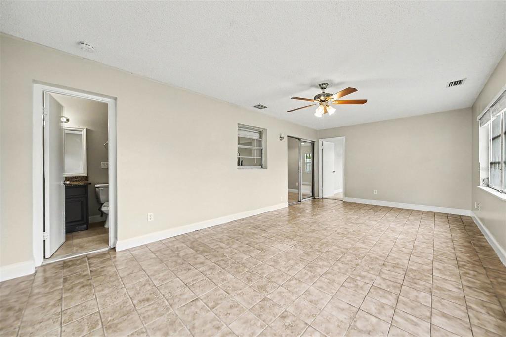 A spacious room features beige tile flooring, a ceiling fan, and an attached bathroom — 140 GUAYMAS DRIVE, KISSIMMEE, FL