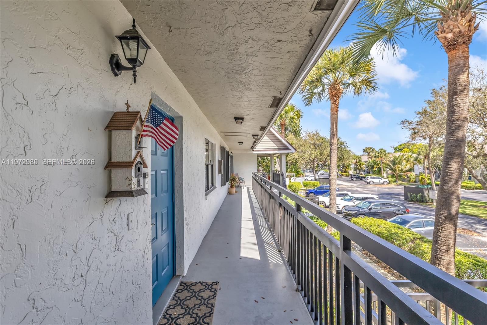 An outdoor walkway features a blue door, a birdhouse, and a metal railing overlooking parking — 3014 SW 21st Ter # 352C, Delray Beach FL 33445, DELRAY BEACH, FL