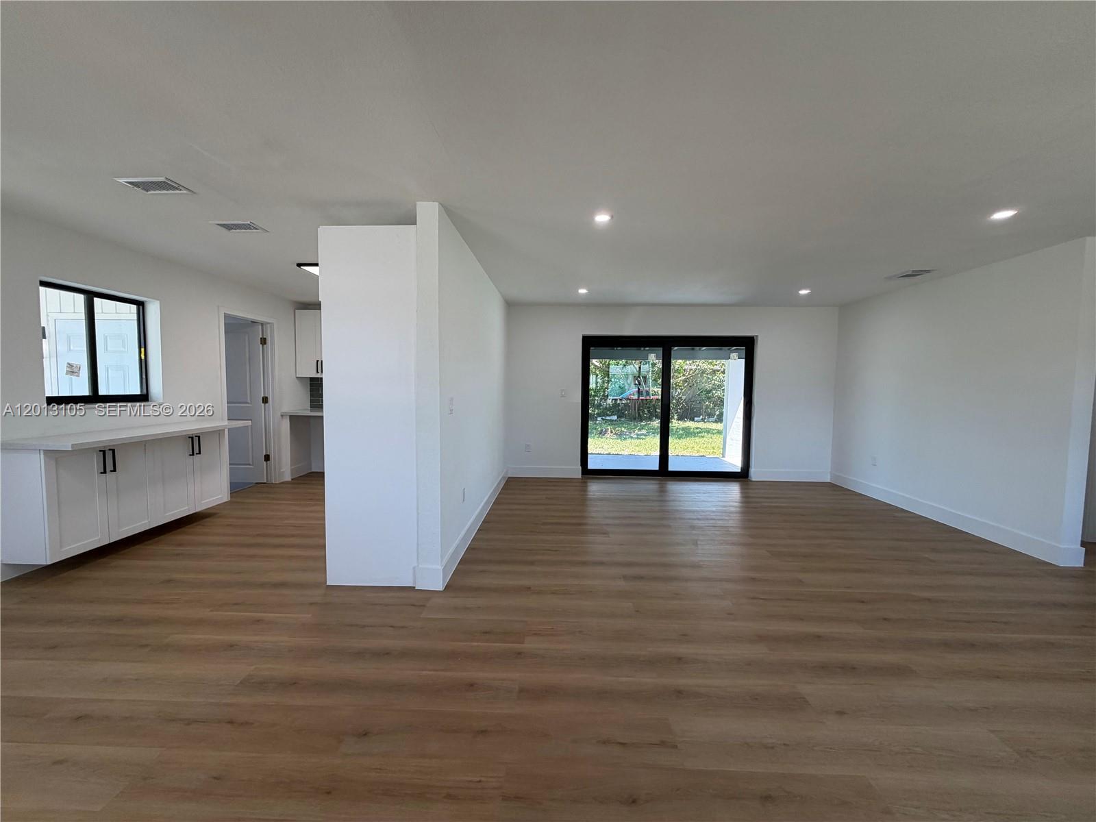 An open-concept living area features light wood-look flooring, white walls, and a sliding glass door — 291 NW 184th Ter, Miami Gardens FL 33169, MIAMI GARDENS, FL